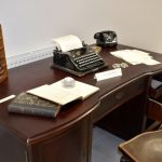 Zabytkowe biurko a na nim liczydło, ksiązki, papiey, okulary i maszyna do pisania